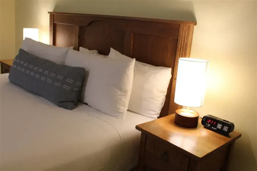Bedroom with a wooden headboard, white bedding, pillows, nightstand with lamp and clock.