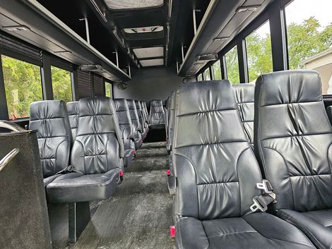 Interior view of a black shuttle bus with rows of black leather seats.
