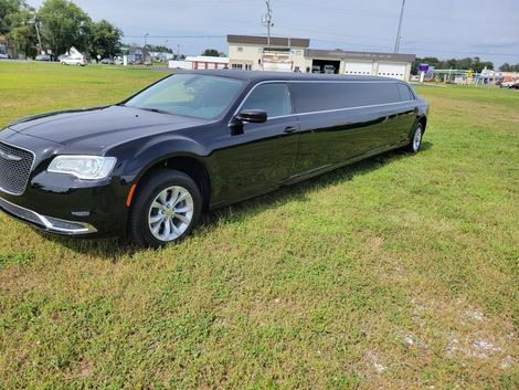 Black limousine parked on a grassy field on a sunny day.