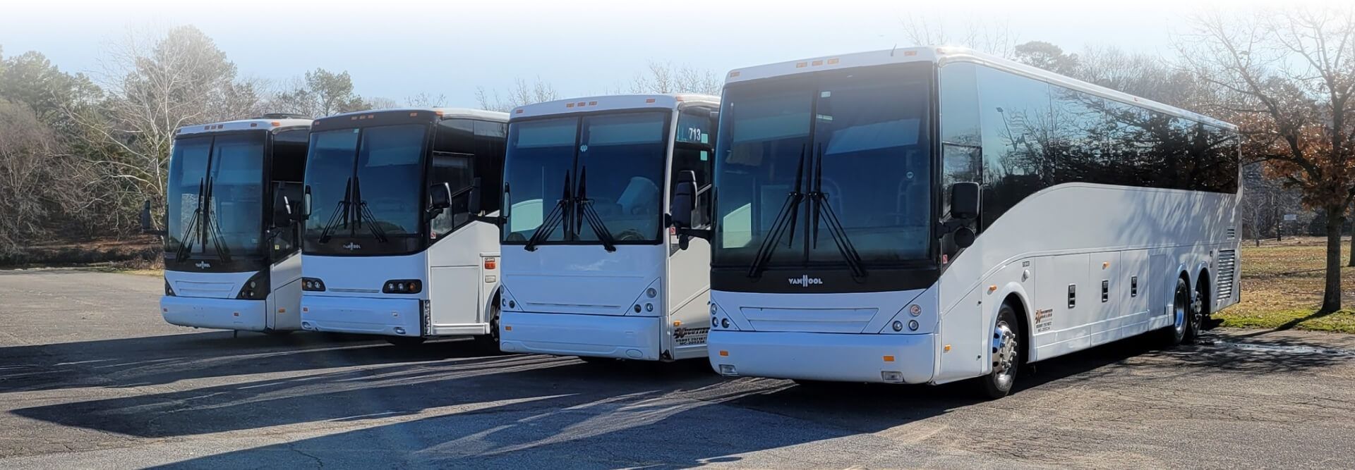 Four white tour buses parked outdoors on a gravel lot.