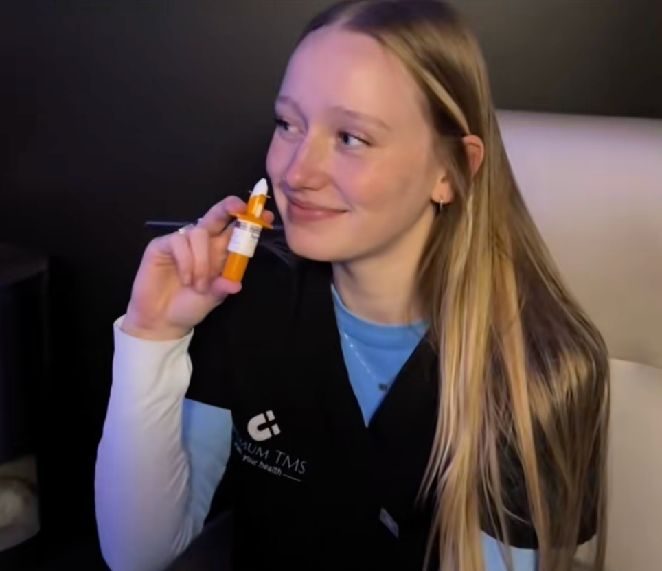 Person holding an orange dropper bottle, smiling in a black jacket against a dark background.