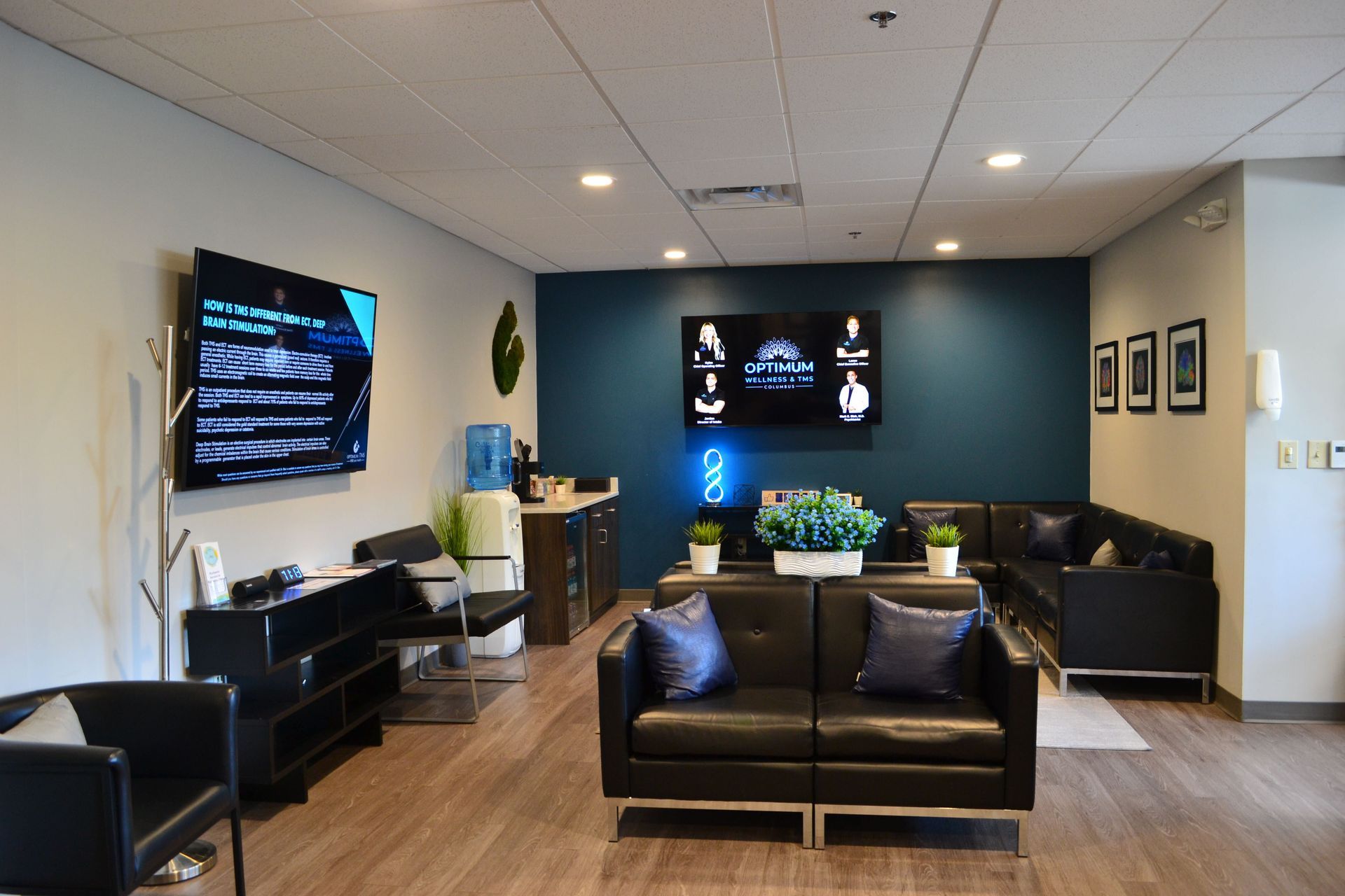 Modern lounge with black couches, wall-mounted screens, and a central coffee table in a waiting area