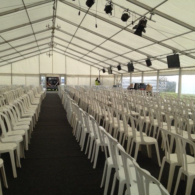 Rows of white chairs arranged inside a large white tent, set for an event.