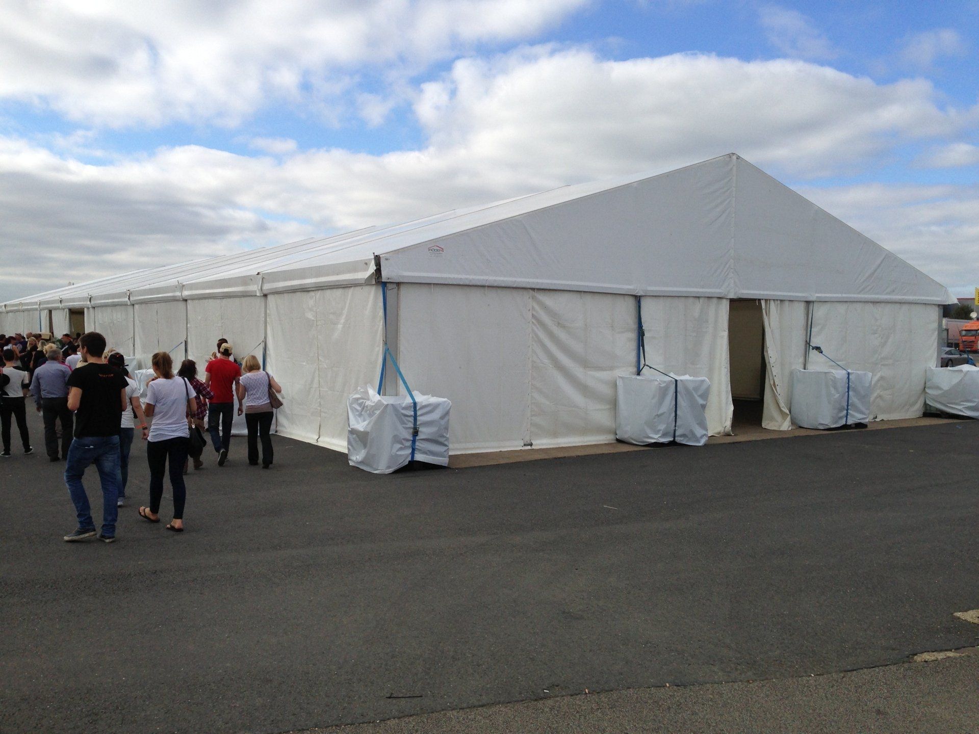 Large white event tent with people walking near entrance, overcast sky.