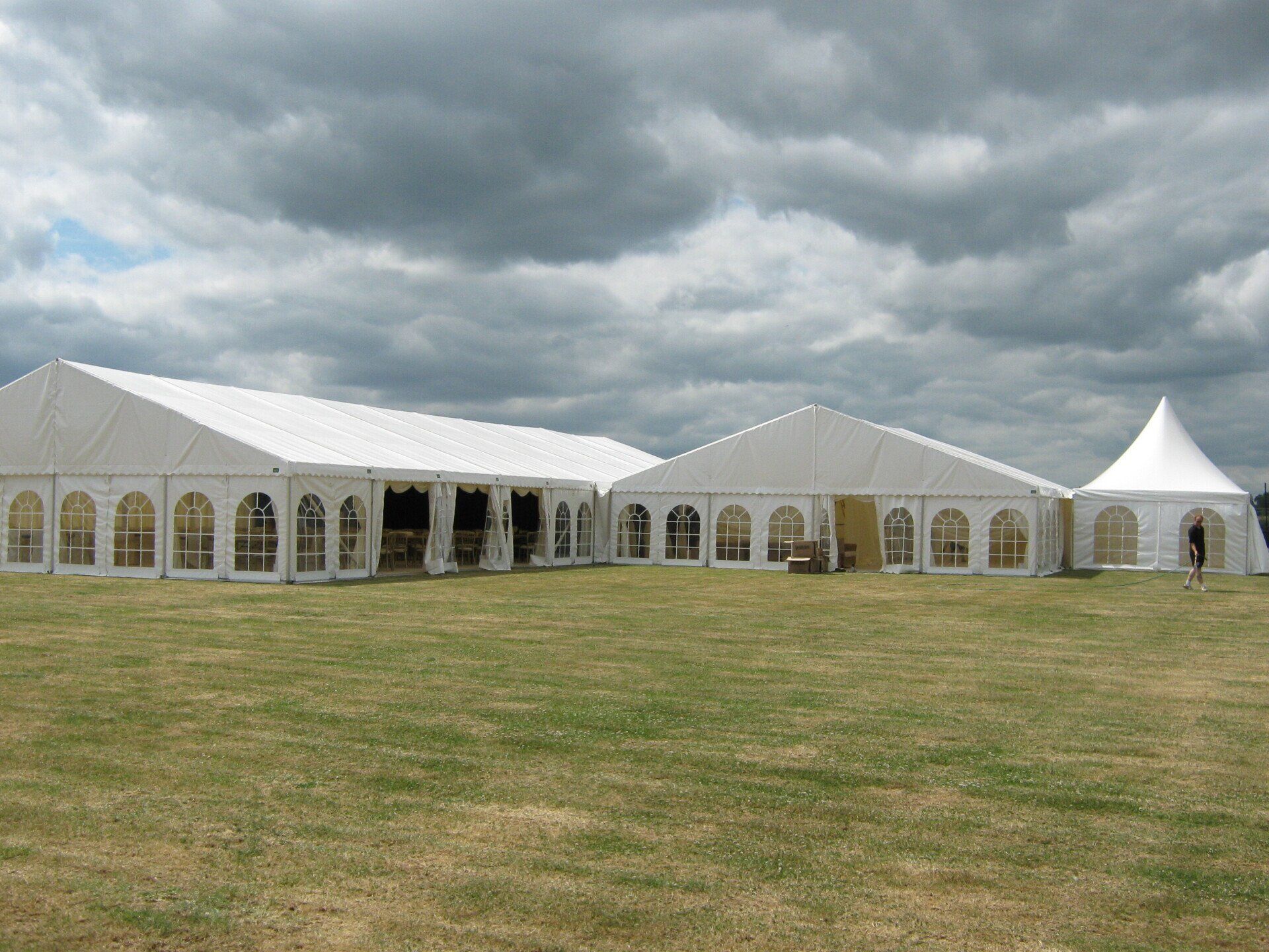 White event tents on a grassy field under a cloudy sky.