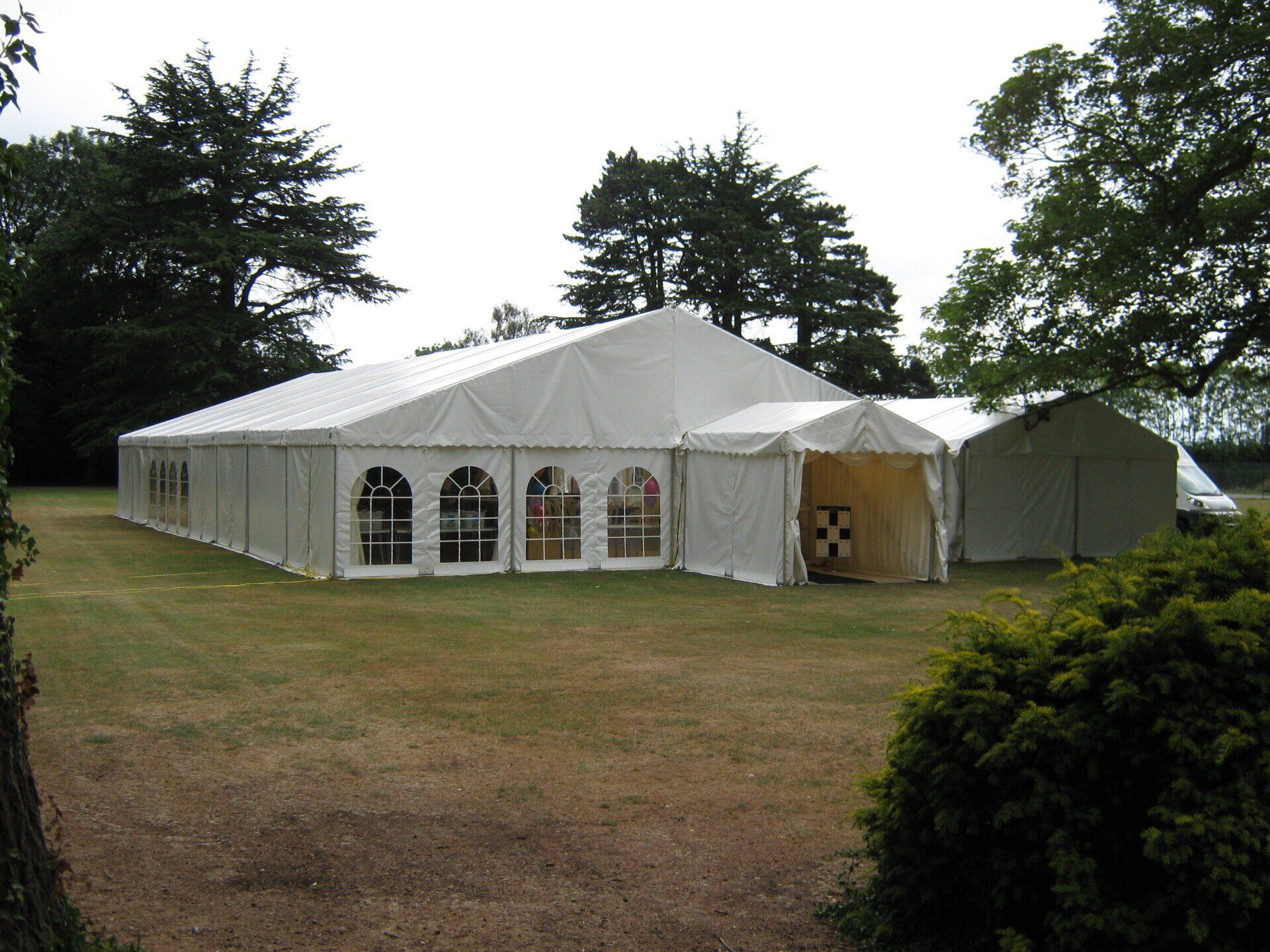 White tent on a grassy lawn; trees in background. Additional smaller tent structures visible.
