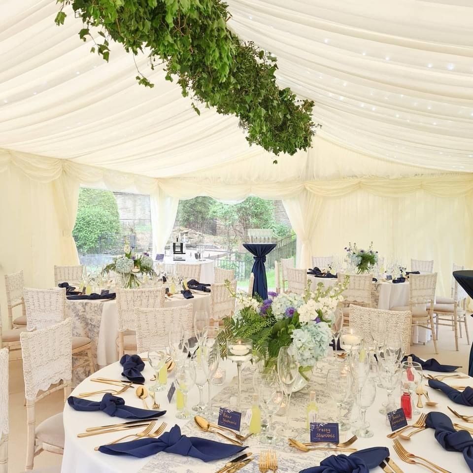 Wedding reception tent with decorated tables, white chairs, and floral centerpieces.