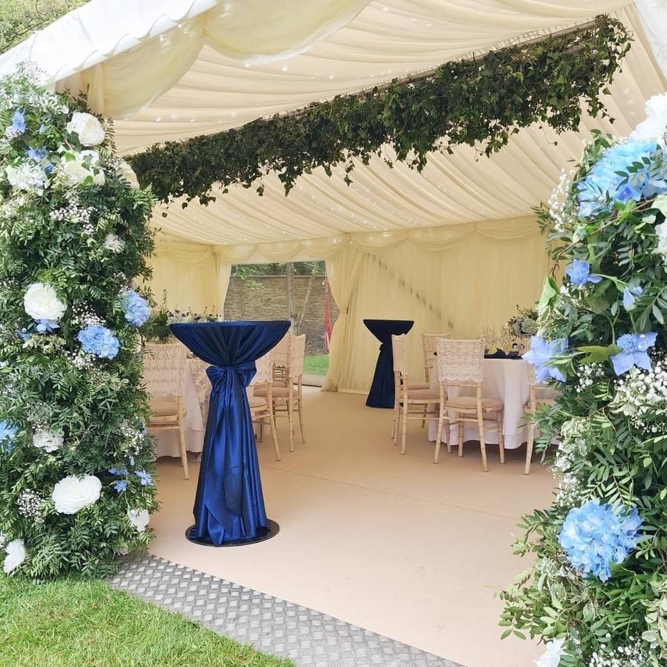 Wedding tent interior with floral archways, high-top tables, and tables with chairs.