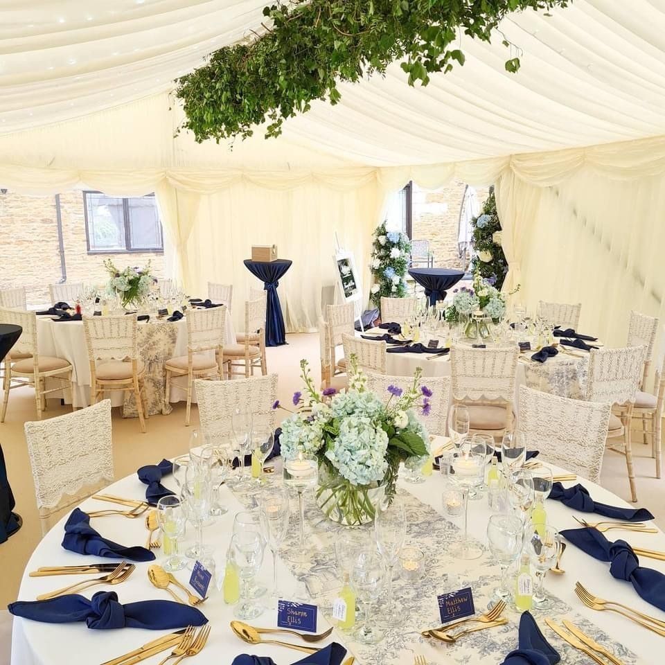 Elegant wedding reception setup under a tent with round tables, flowers, and navy blue accents.