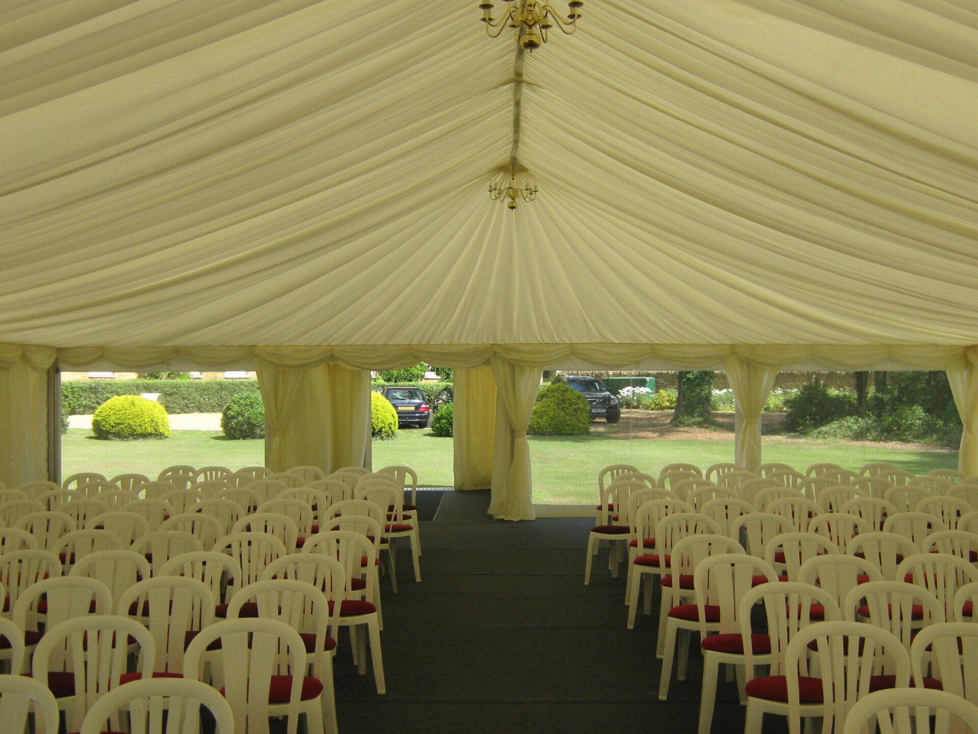 Rows of white chairs inside a large tent, green lawn visible through windows.