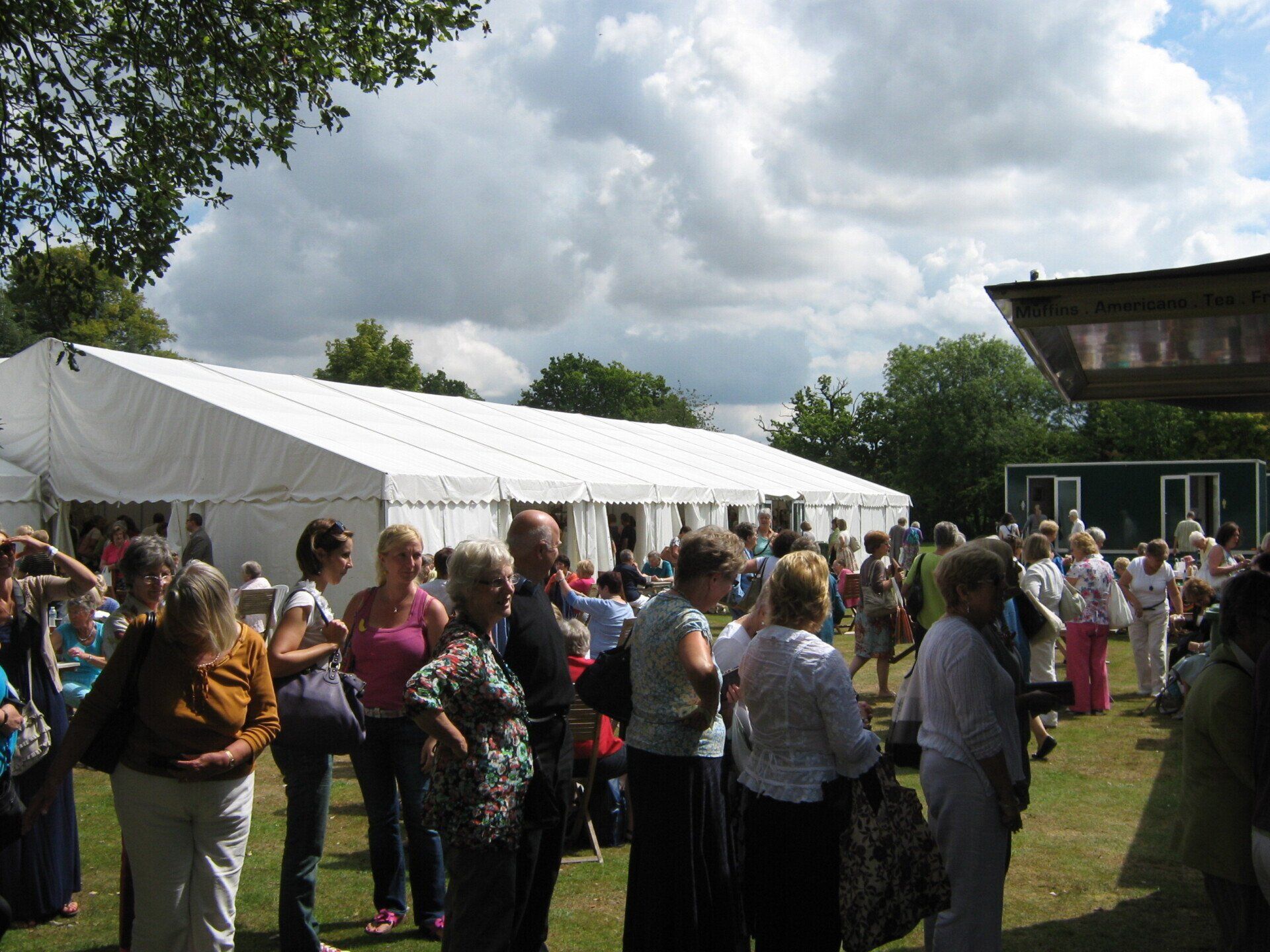 People gathered outdoors near a large white tent under a cloudy sky.