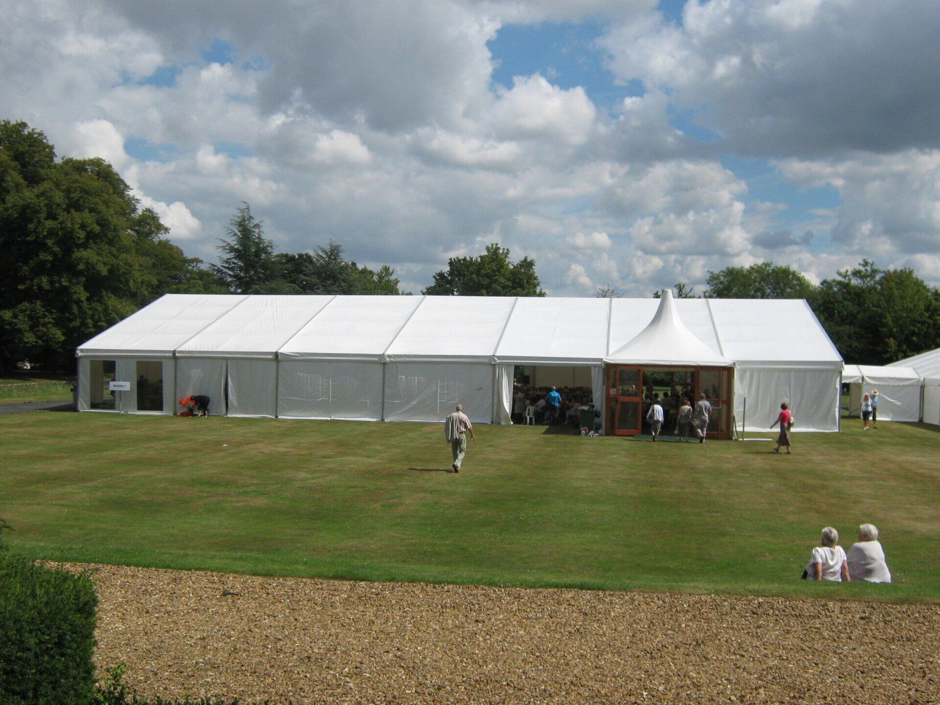 White event tent on a grassy lawn; people gather outside.