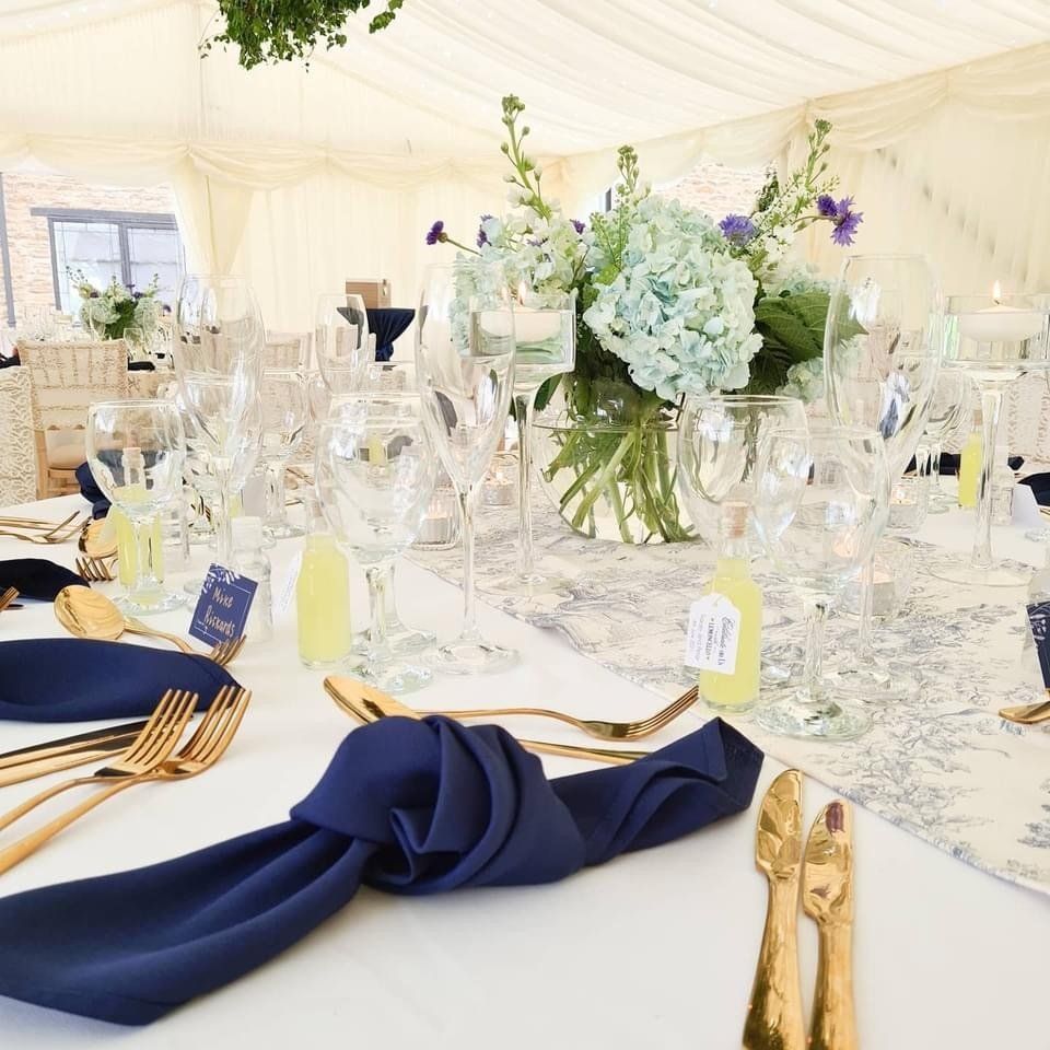 Elegant wedding table setting with blue napkins, gold cutlery, and floral centerpiece.