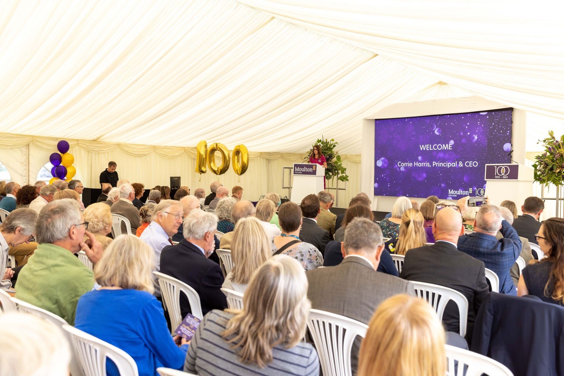 Audience seated inside a tent, facing a large screen displaying 