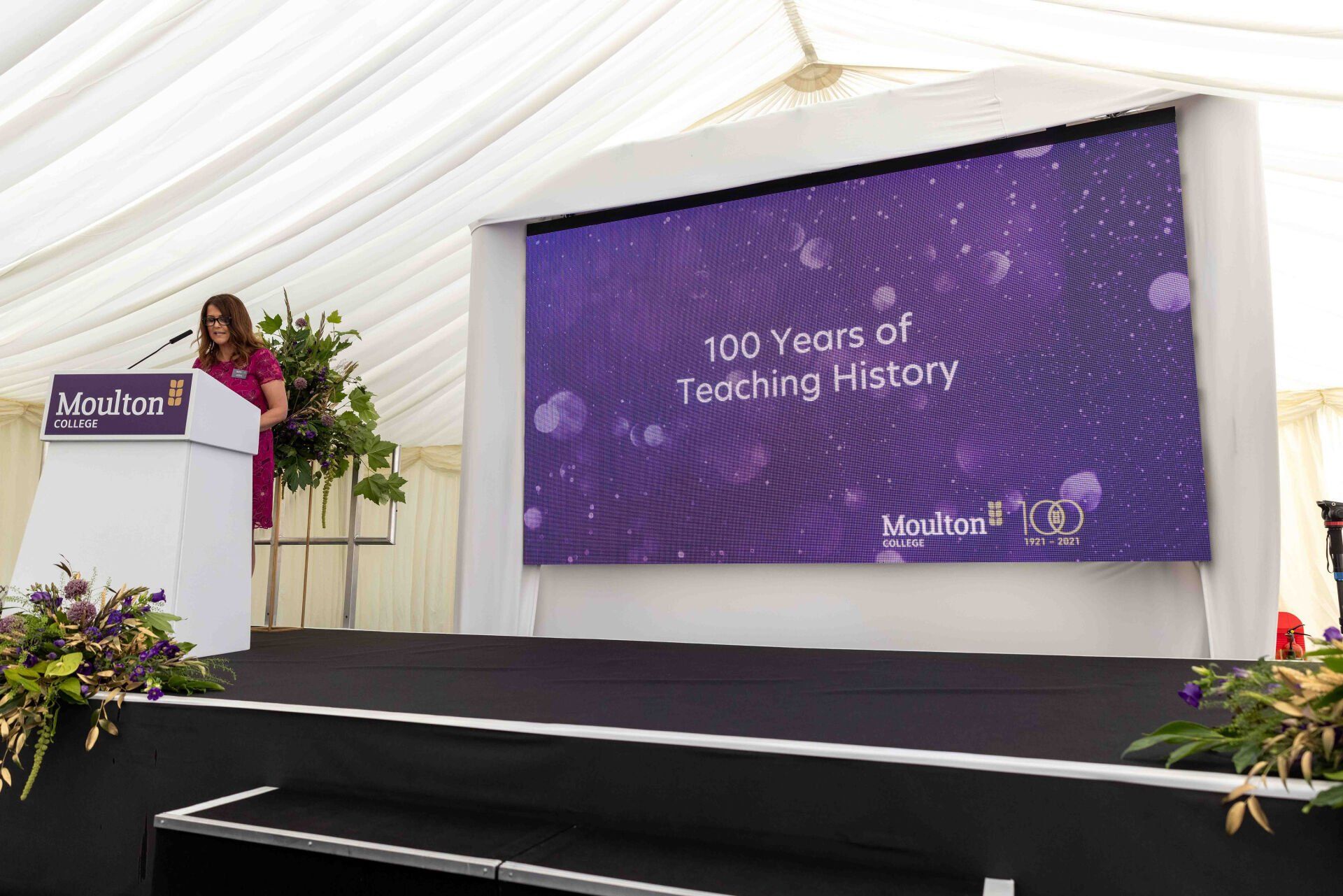 Woman at podium speaking in front of a screen with 