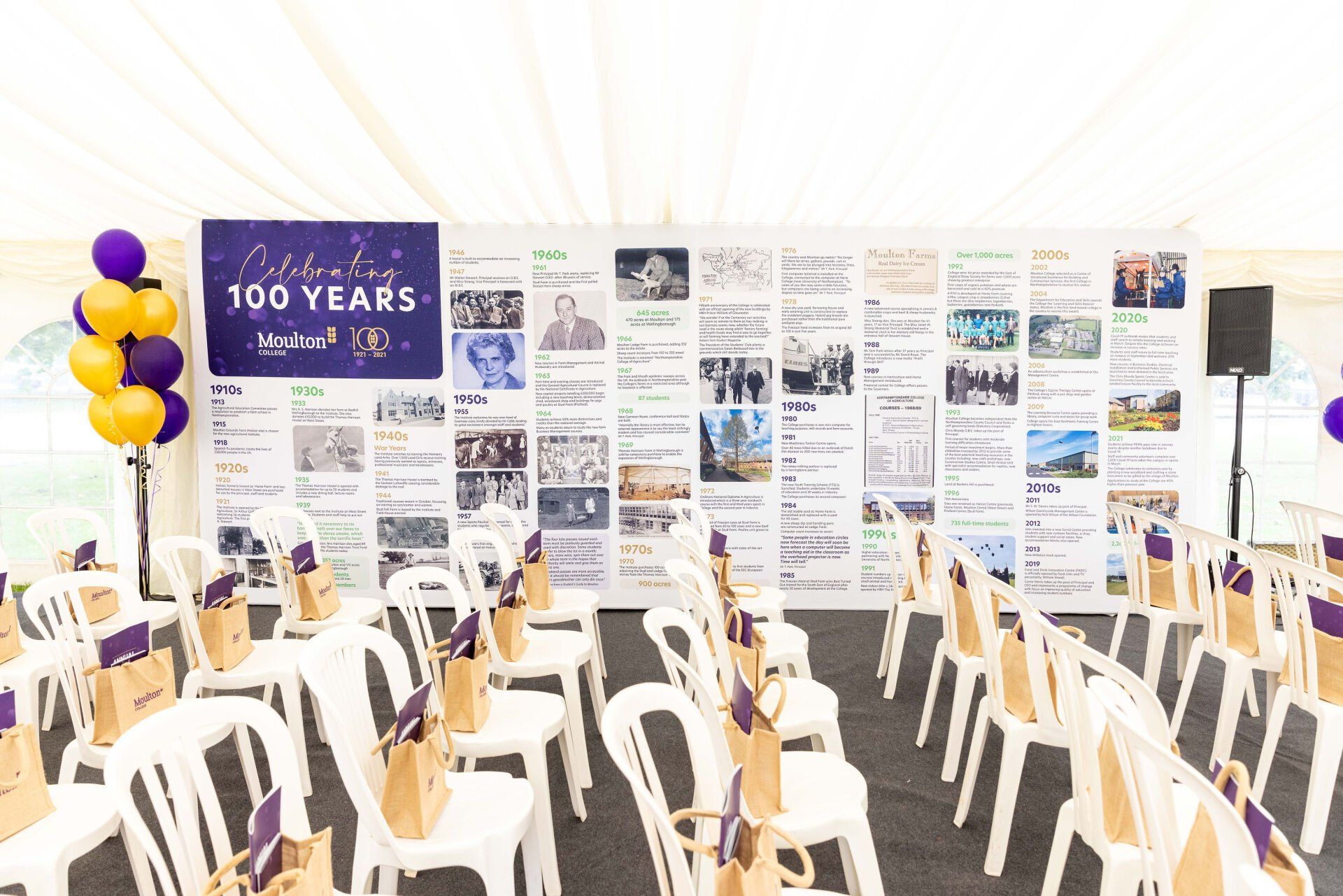 Event tent with rows of chairs facing a timeline display and balloons. Purple and gold color scheme.