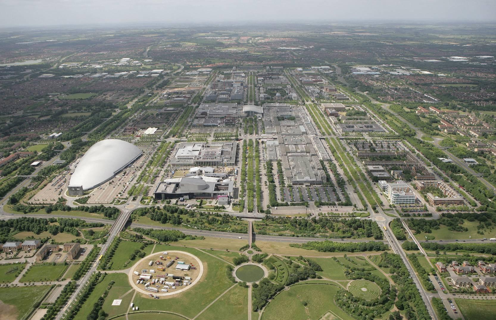 Aerial view of Milton Keynes, UK, showing central grid streets, business parks, stadium, and parkland.