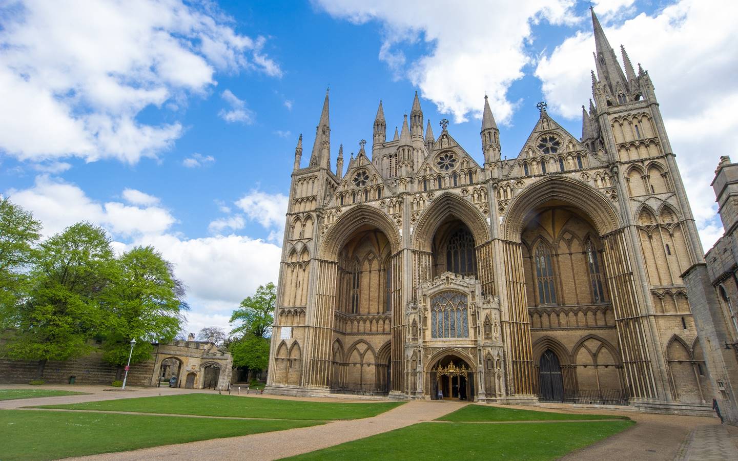 Gothic cathedral facade with arched entrance, spires, and a blue sky with clouds. Green lawn in front.