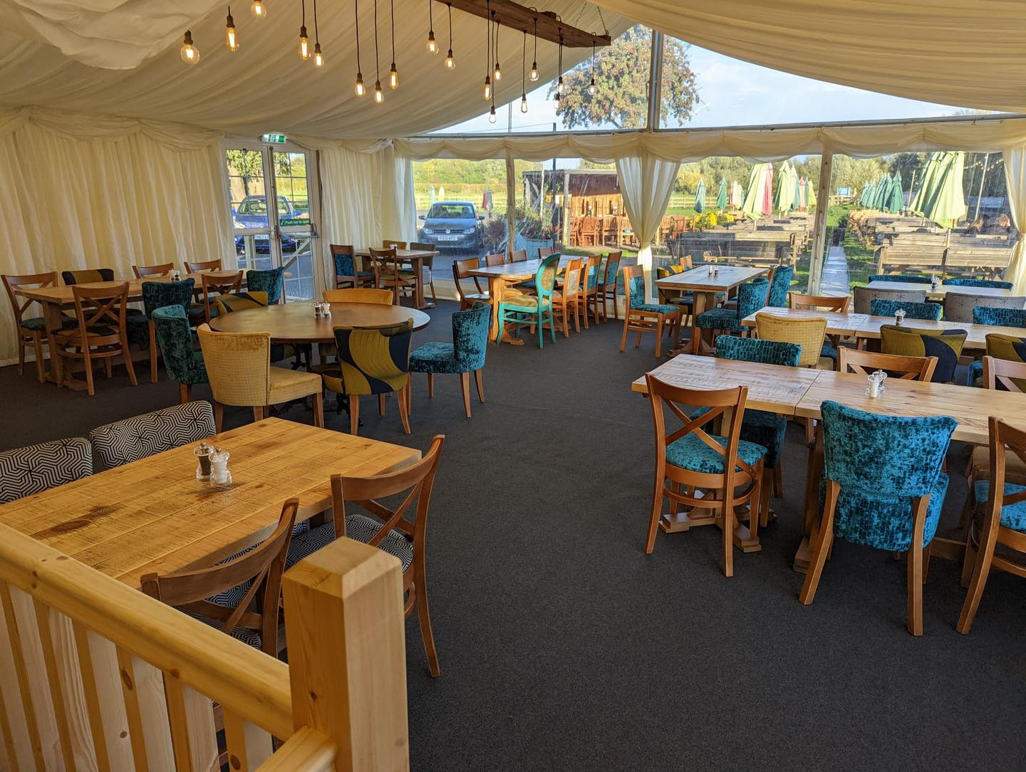 Interior of a large tented dining area with tables and chairs, natural light, and outdoor view.
