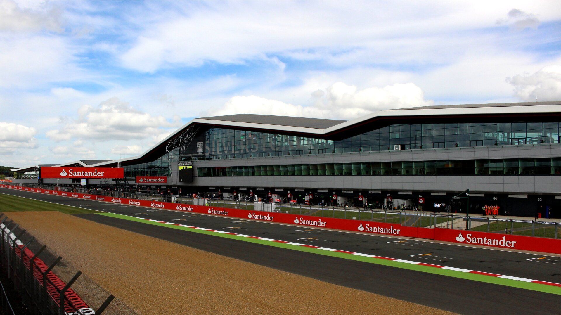 Race track with a long building, red and white banners, and a cloudy sky.