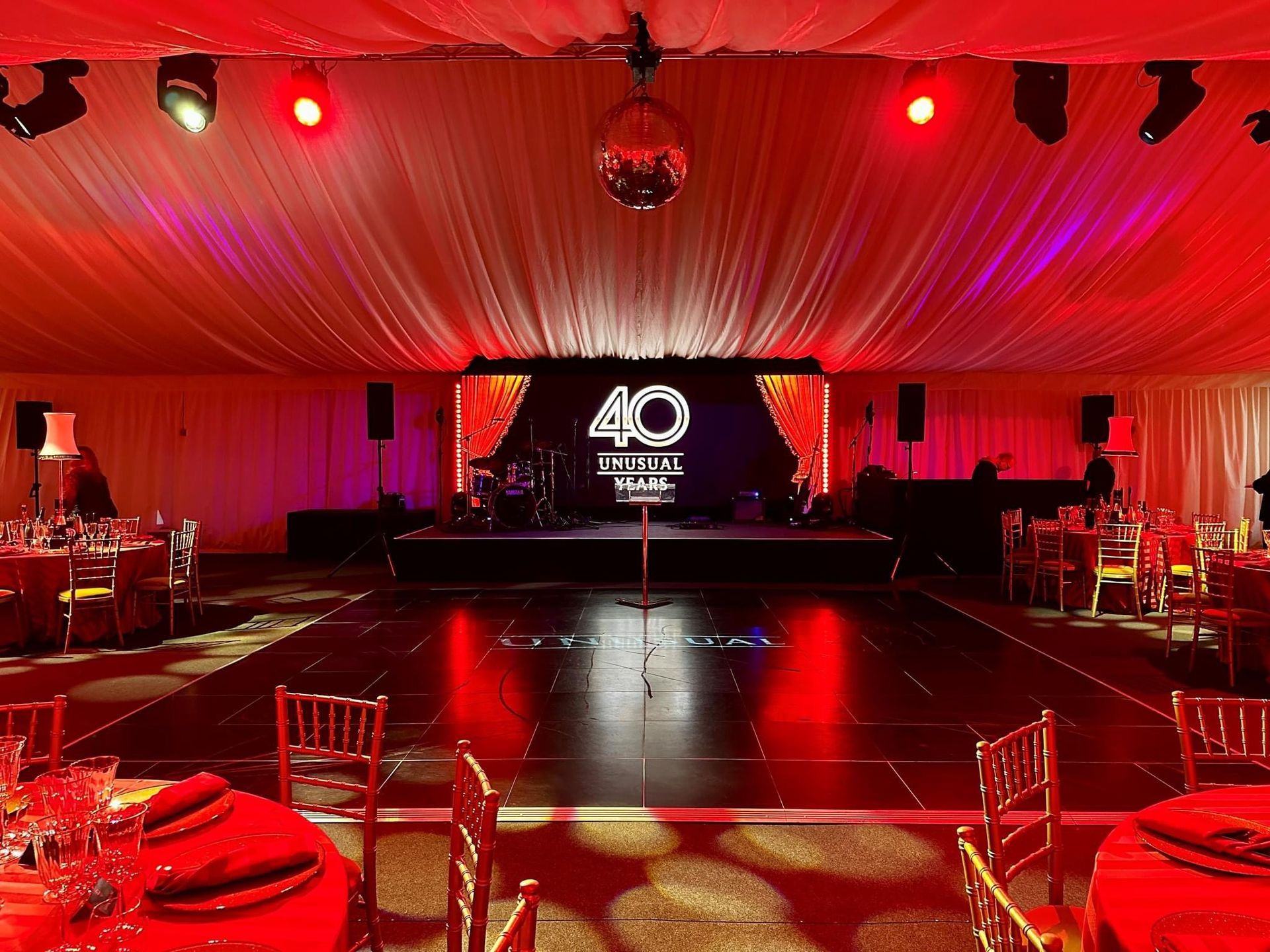 A red-lit event venue with a stage, dance floor, tables, and a disco ball. Celebrating a 40-year anniversary.