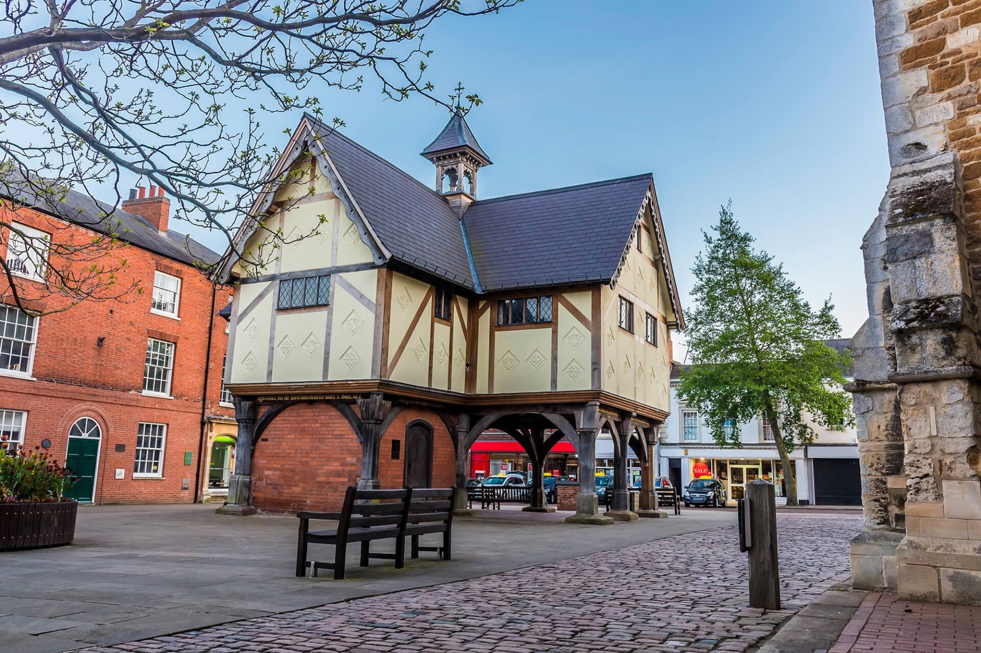 Marquee Hire in Market Harborough Tudor style building on cobblestone, with benches. Other buildings and trees are in view.