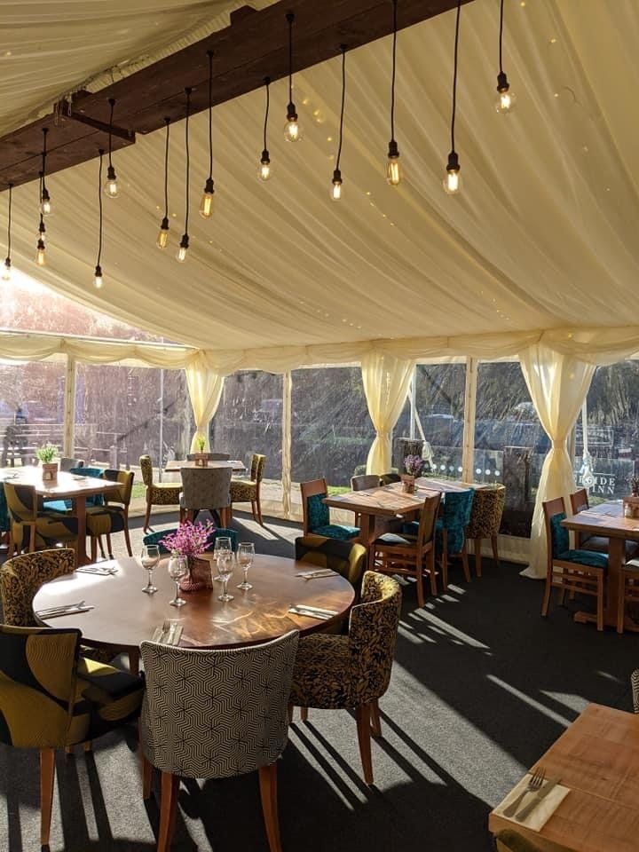 Restaurant interior with round tables, various patterned chairs, and hanging lights under a draped ceiling.
