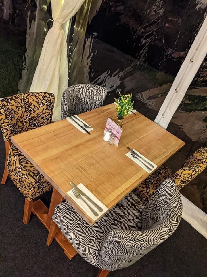 Table set for dining with patterned chairs, under a transparent tent.