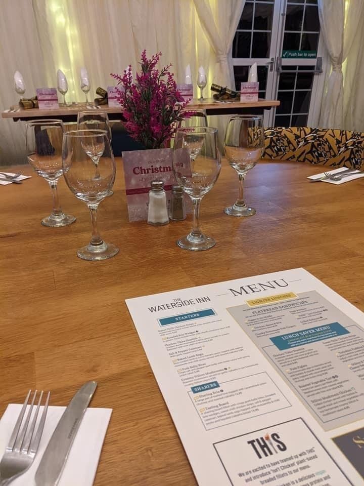 Dining table set for a meal at Waterside Inn with wine glasses, menu, flowers, and Christmas decor.