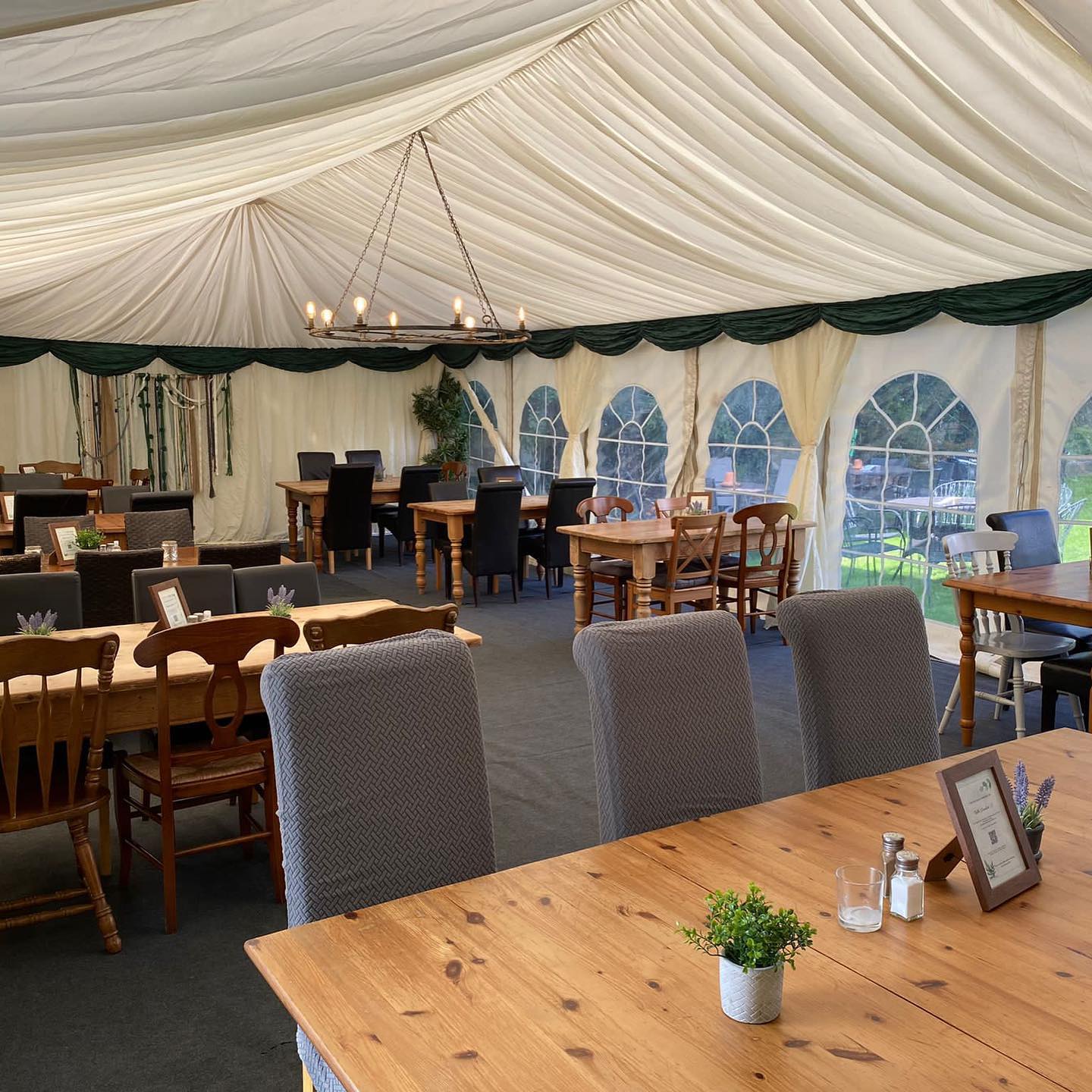 Interior of a tent used as a dining area with tables, chairs, and greenery.