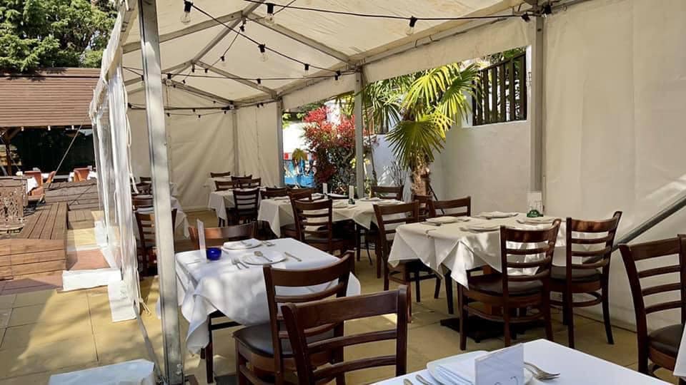 Outdoor dining area under a white tent, tables set with white tablecloths and chairs.
