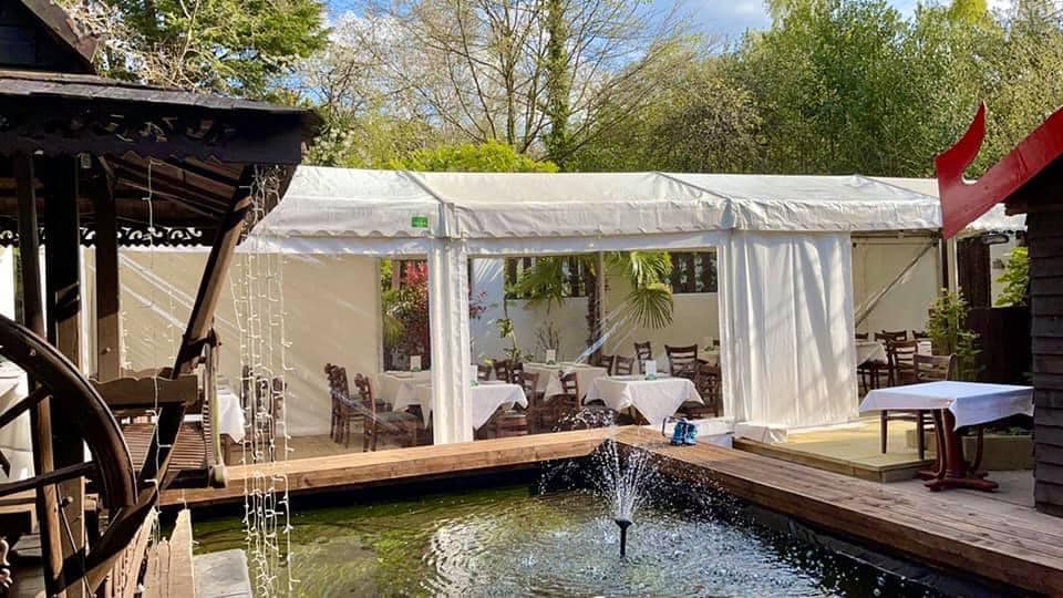 Outdoor restaurant setting with covered dining area next to a water feature with a fountain.