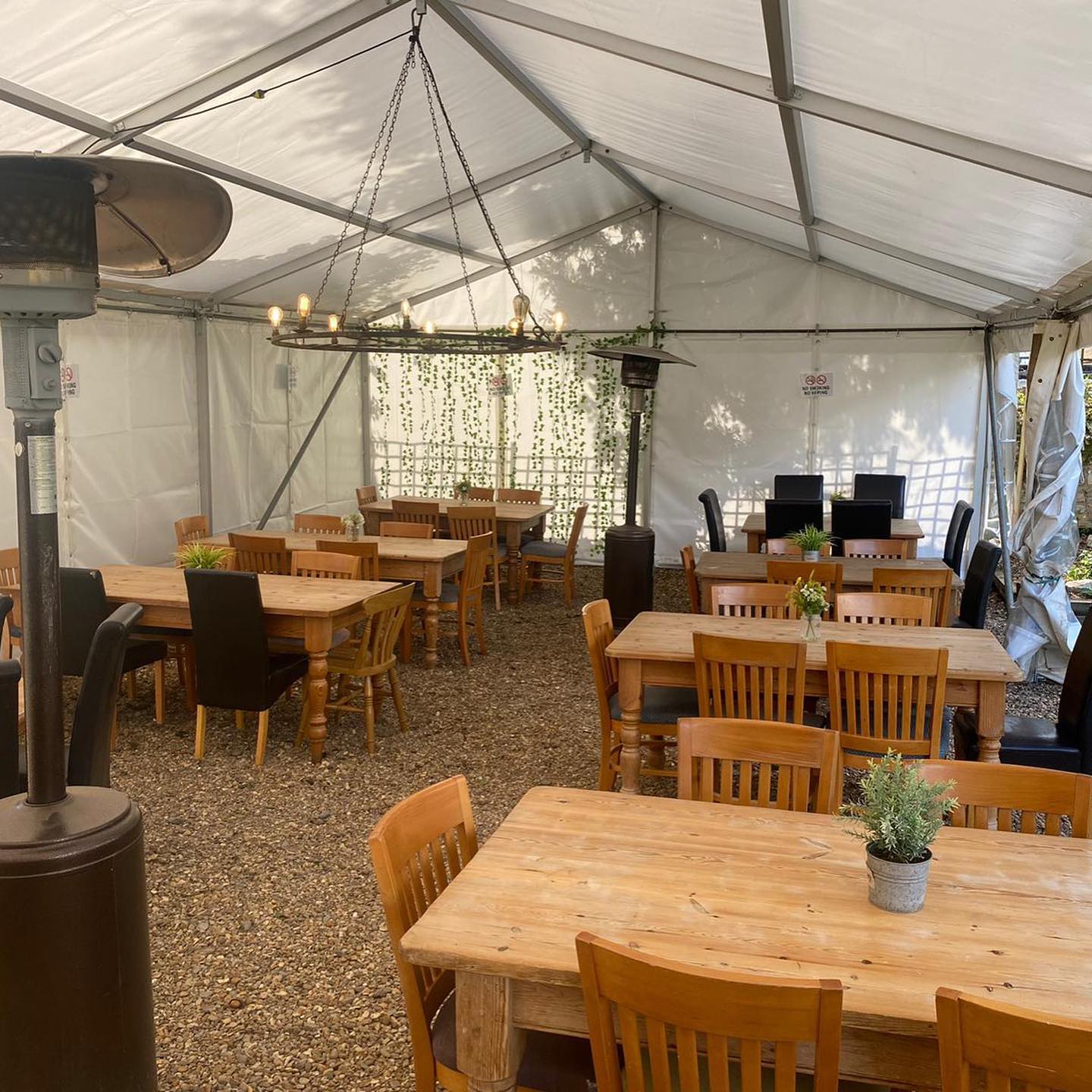 Outdoor dining area inside a white tent with tables, chairs, and a heater.