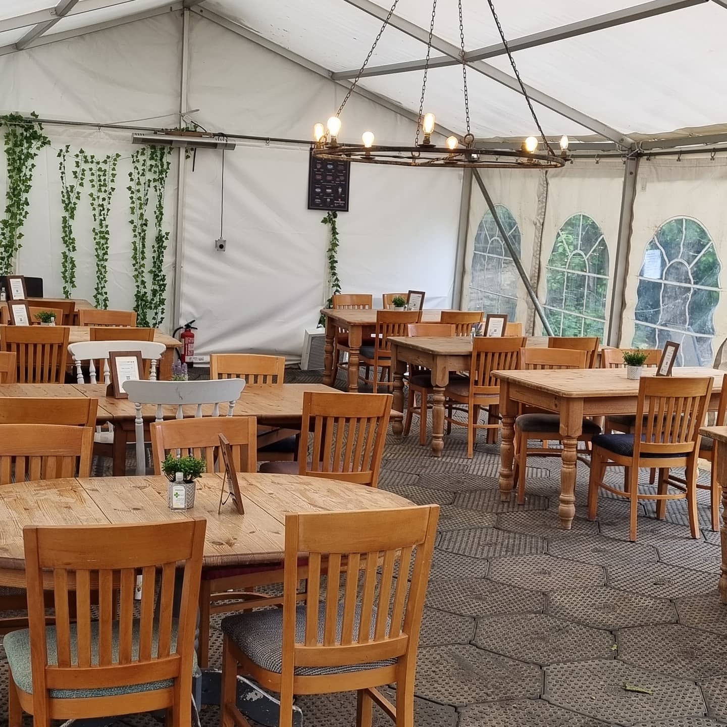 Tables and chairs inside a tent, possibly a restaurant or event space. Natural light, wooden furniture.
