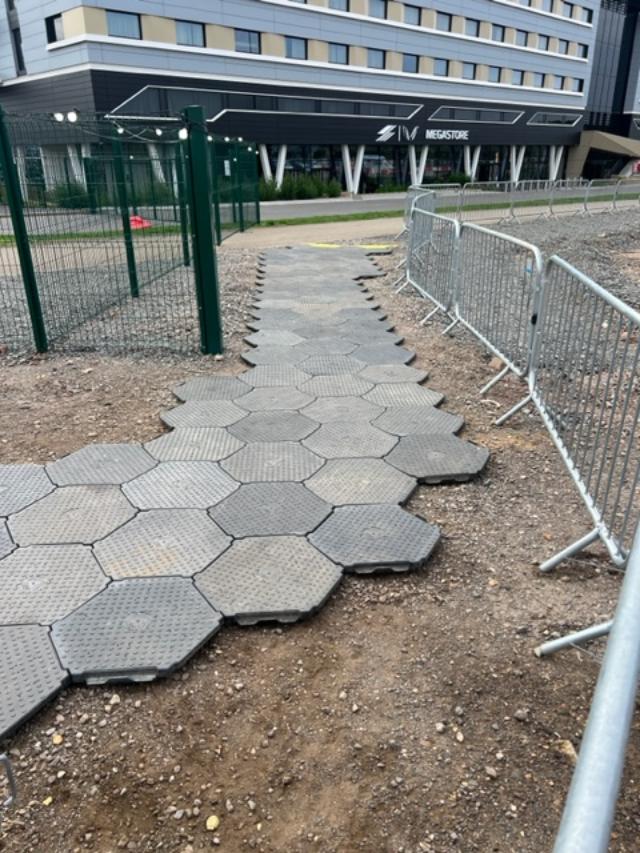 Hexagonal pavers forming a path through dirt, near a building and temporary fencing.