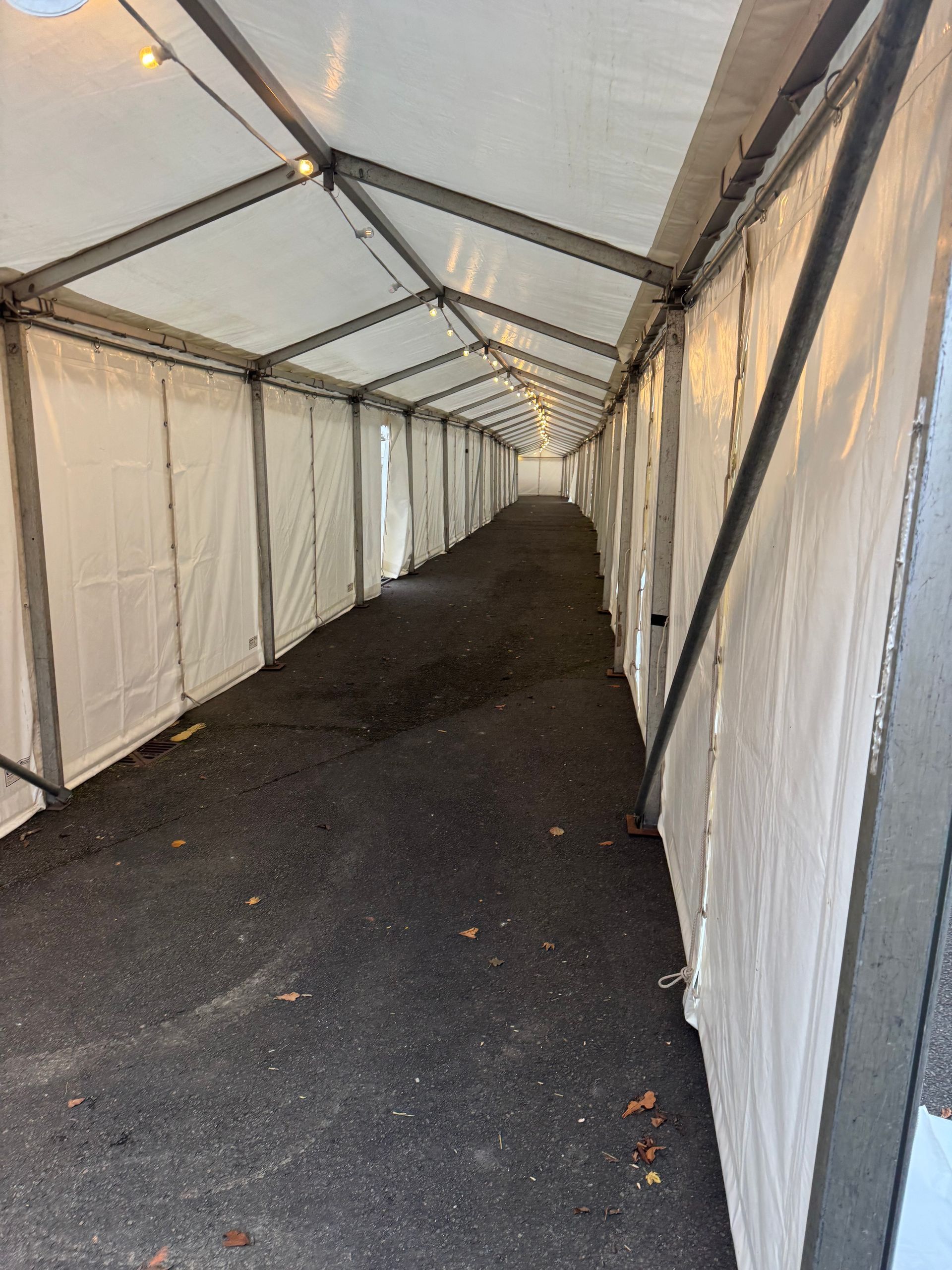 Long, covered walkway with white walls and a dark asphalt floor.