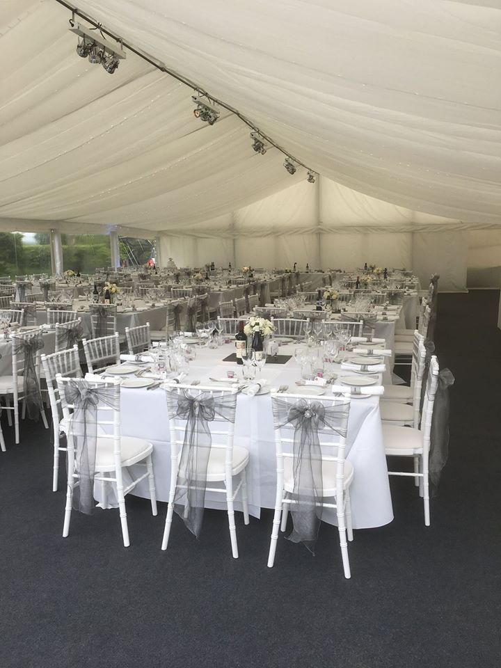 Wedding reception tent with white tables and chairs, decorated with grey accents.