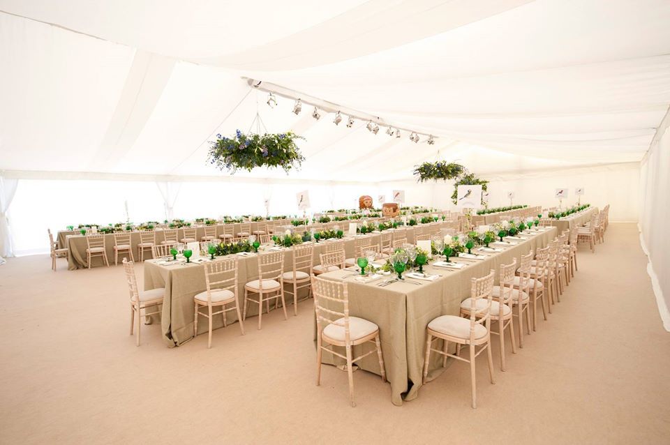 Elegant tented reception. Long tables set with cream linens, green centerpieces, and white chairs.