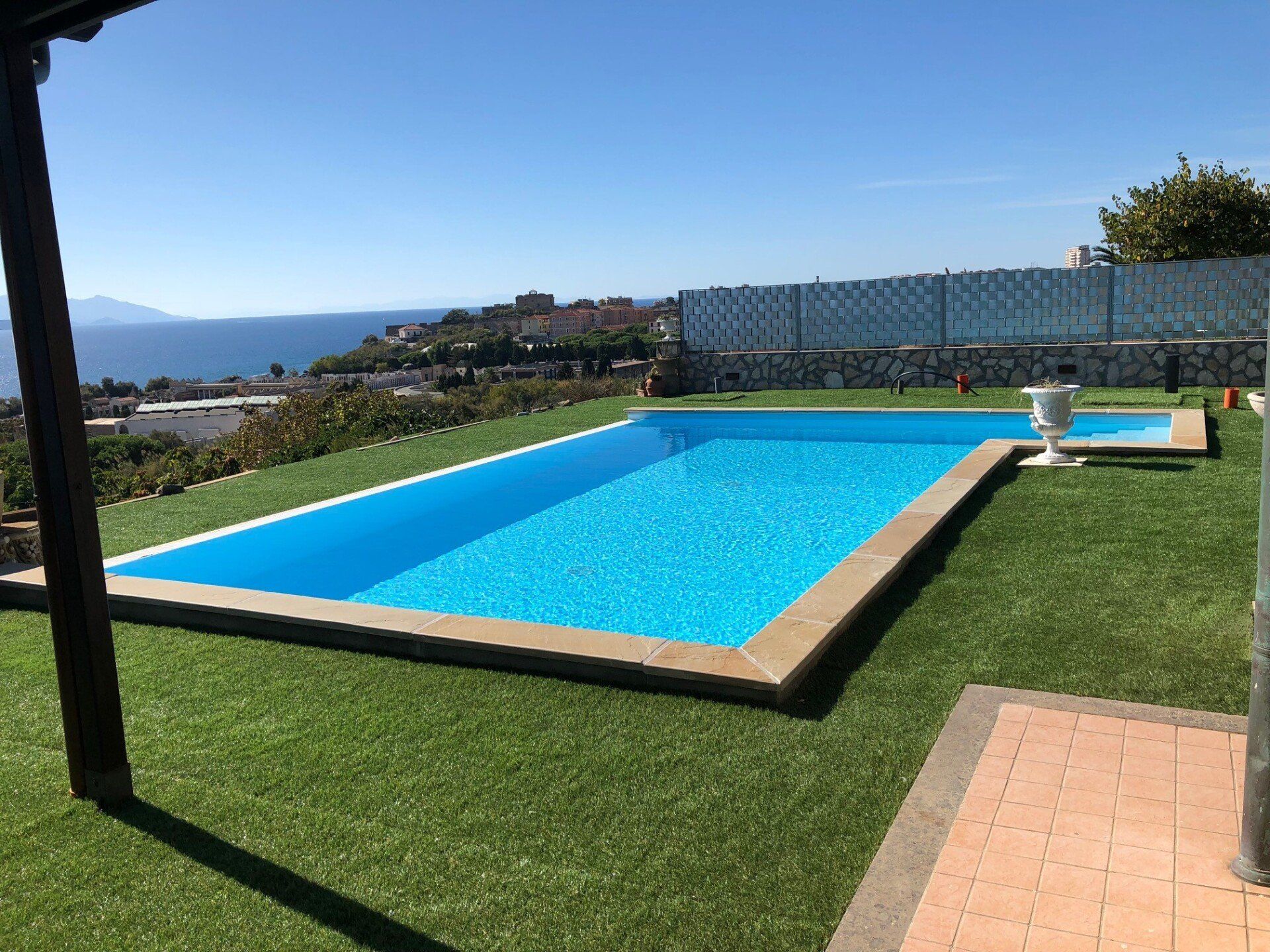 Una piscina rettangolare dalle acque di un azzurro brillante si erge su un prato verde, affacciata su una città
