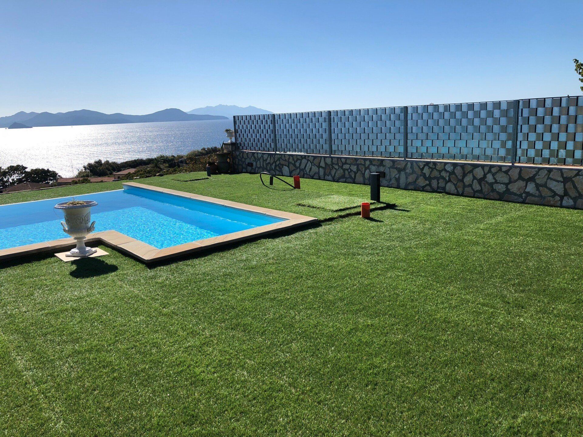 Una piscina situata in un prato con vista sul mare e una recinzione decorata sullo sfondo.