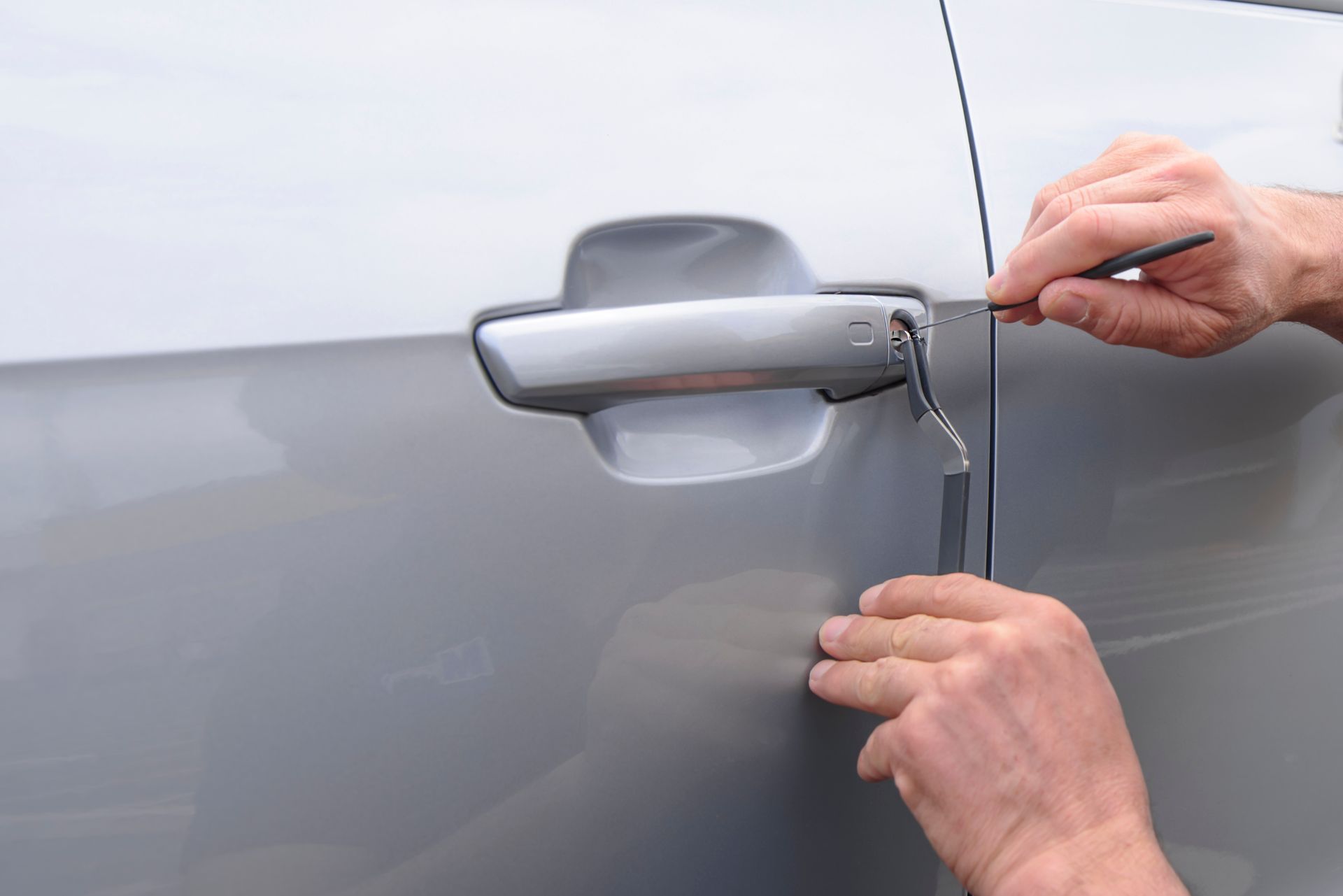 Hands using a tool to unlock a car door.