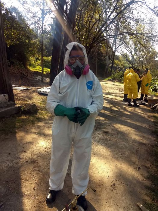 Un hombre vestido con un mono blanco y una máscara de gas está parado en un camino de tierra.