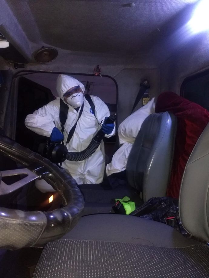 Un hombre con un traje de protección está rociando un automóvil con un pulverizador.