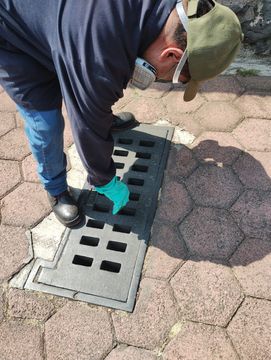 Un hombre que lleva una máscara está limpiando la tapa de una alcantarilla en el suelo.