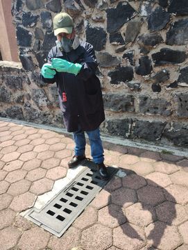 Un hombre que lleva una máscara y guantes está de pie junto a la tapa de una alcantarilla.