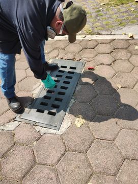 Un hombre está limpiando una tapa de alcantarilla en la acera.