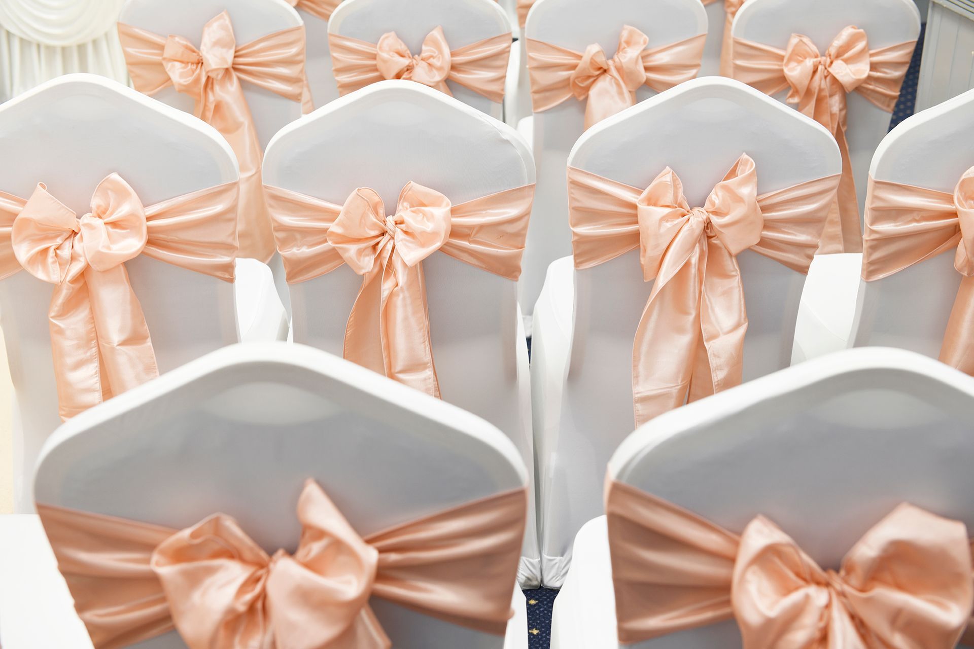 A row of white chairs with pink bows on them.