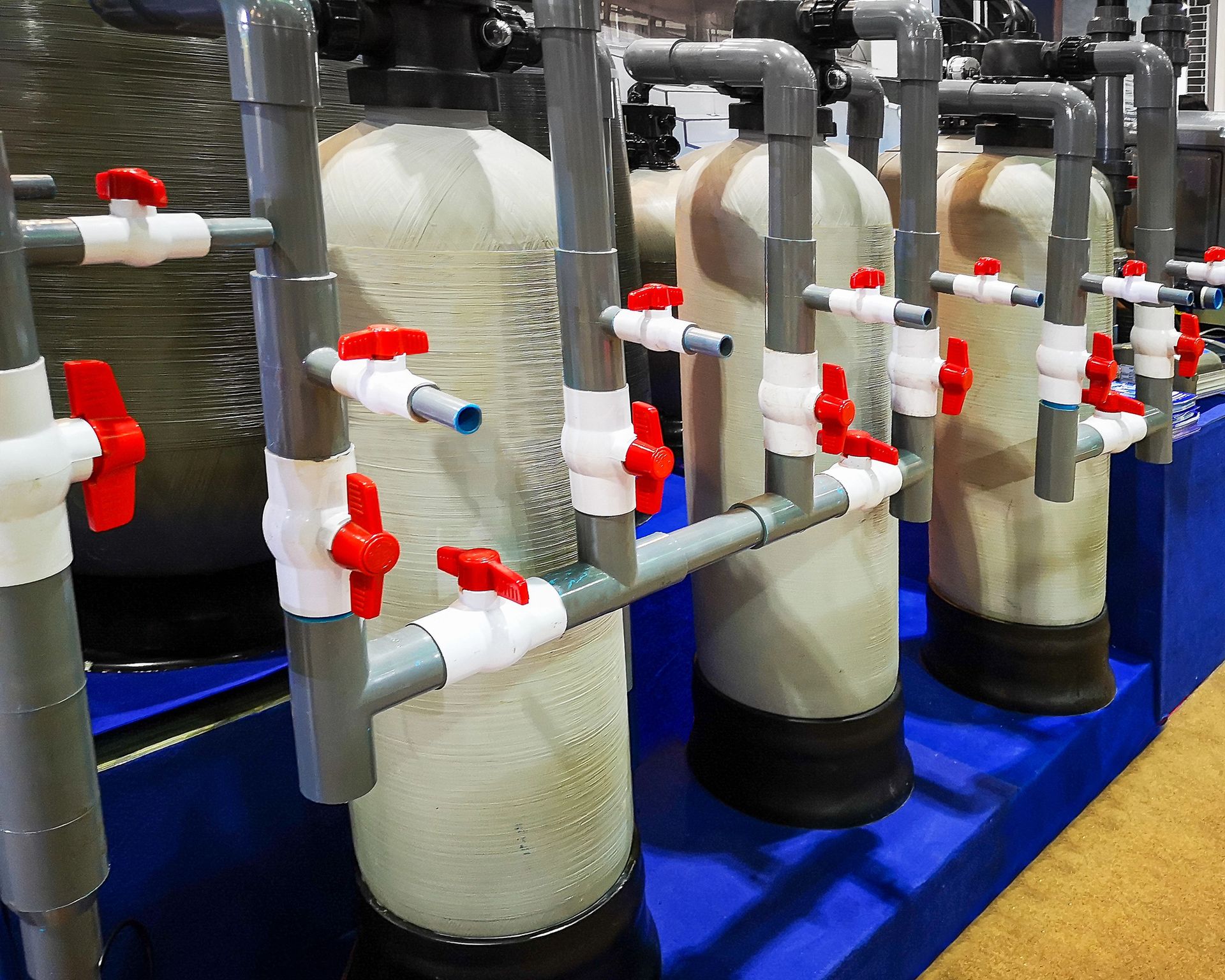 Gloved hands adjusting white PVC pipes and valves beside a blue tank outdoors