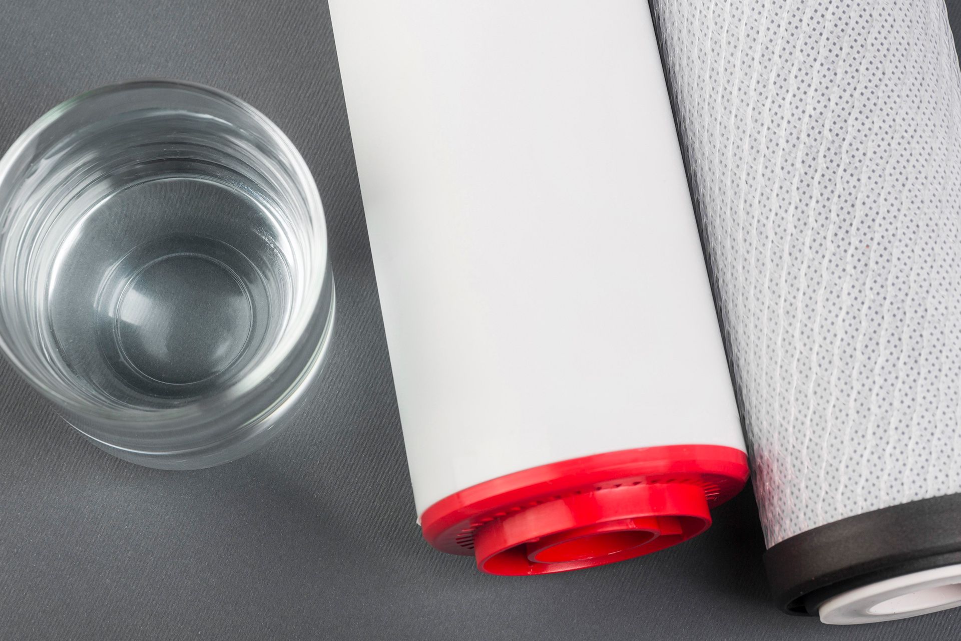 Glass of water next to two white water filter cartridges with red and black accents.