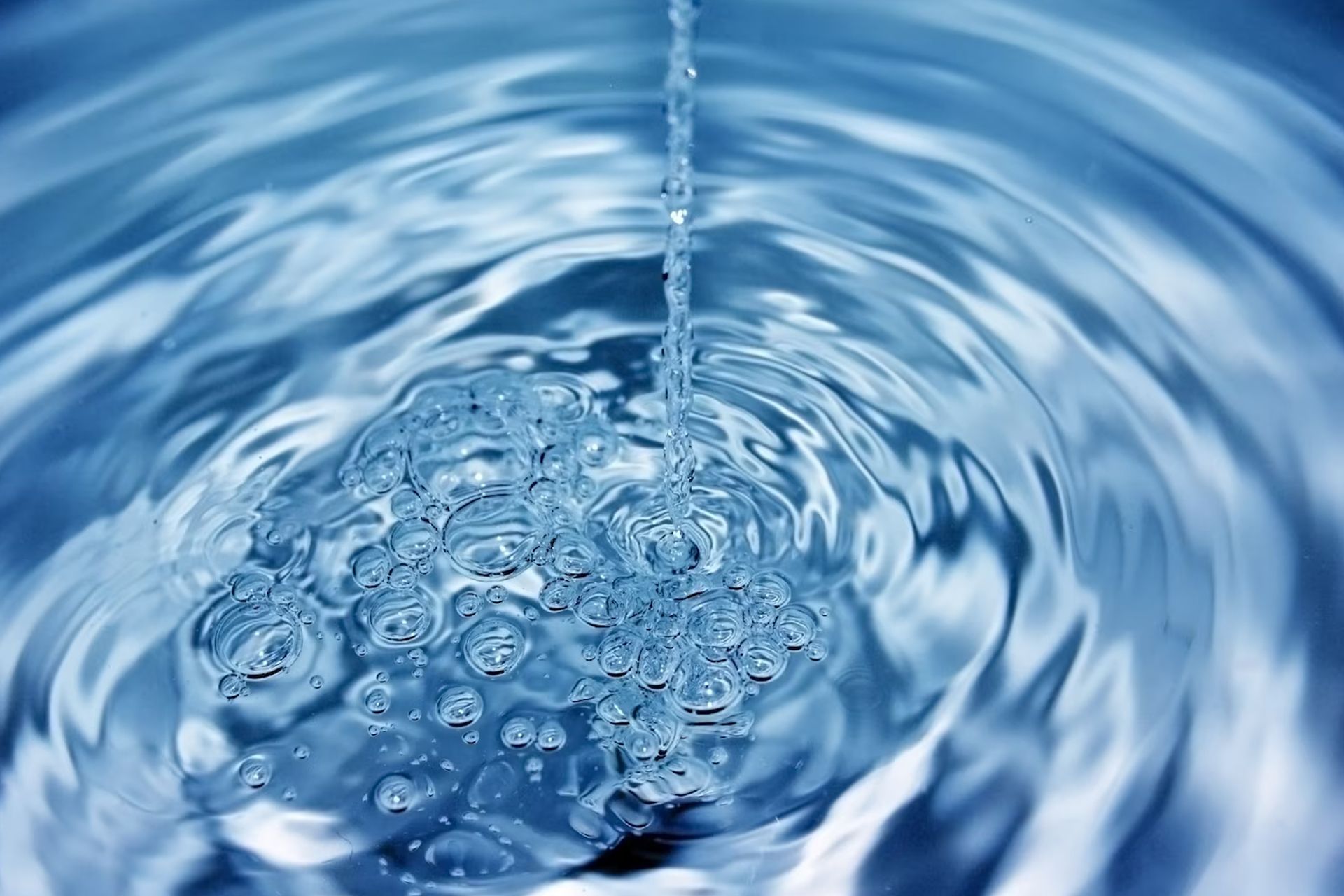Water pouring into a body of water, creating bubbles and concentric ripples; blue hues.